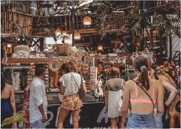People shopping at a rustic boutique with wooden structures, palm leaves, and warm lighting
