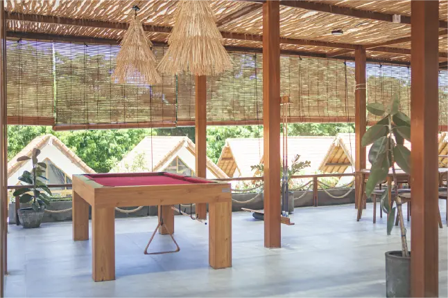 Pool table with red felt in an open-air tropical lounge overlooking thatched-roof bungalows