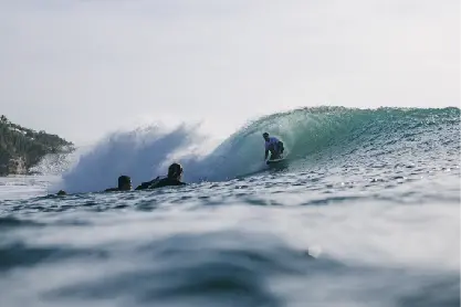 A surfer riding inside a breaking barrel wave as others watch from the water