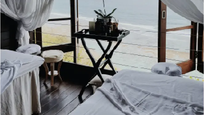 Spa treatment room with massage tables and a view of the ocean through large open windows