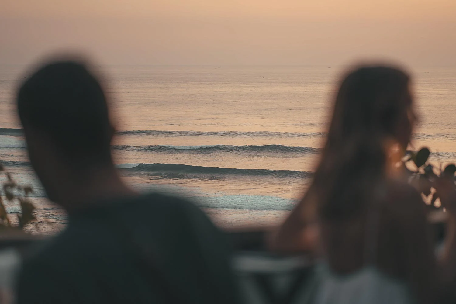 Ocean waves rolling toward the shore at sunset, framed by the blurred silhouettes of two people