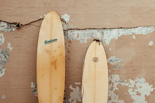 two old surfboard leaning on a wall in need of a ding repair or surfboard insurance.